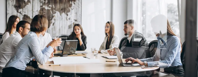 Imagen: Mesa redonda con 8 personas conversando sobre la administración de proyectos de la empresa.