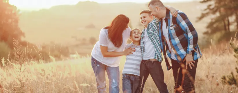 Familia de 4 personas abrazados en una pradera