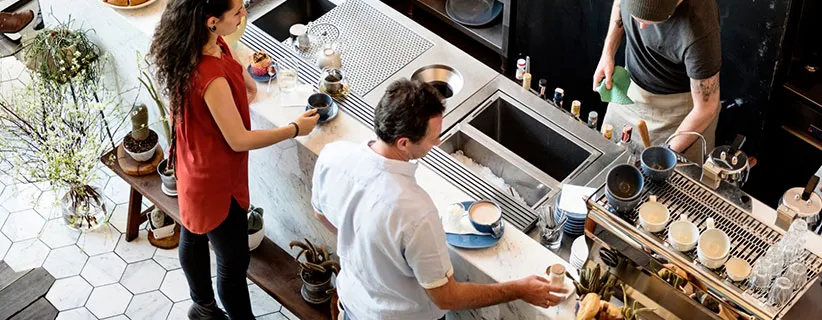 Imagen: Pareja frente a mostrador en espera mientras cocineros les preparan la orden en un local comercial