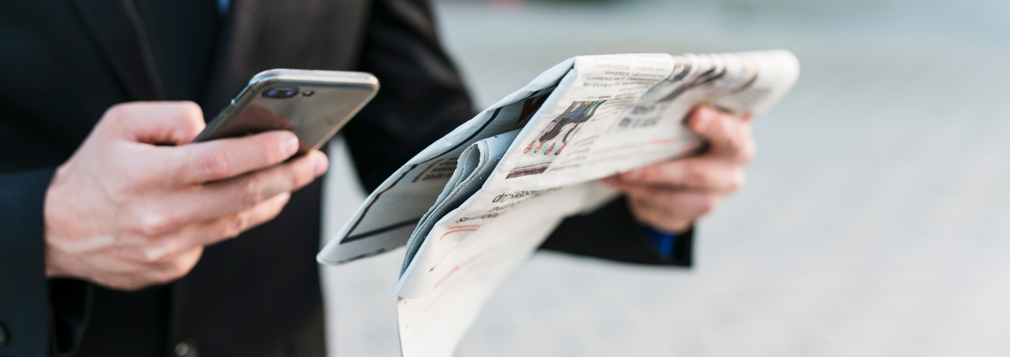 Persona leyendo el periódico mientras utiliza su celular