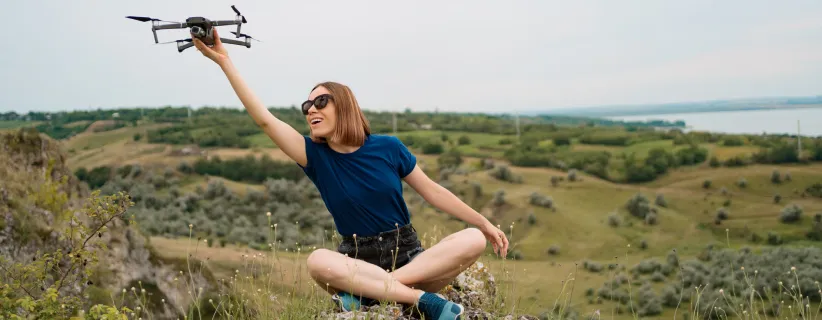 Mujer sentada en  una colina sosteniendo un dron con su mano derecha