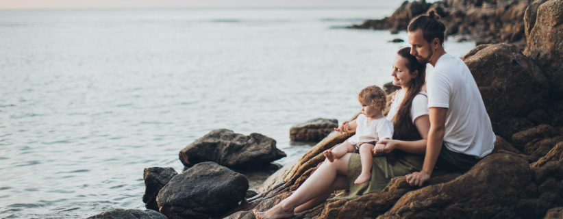 Familia de 3 personas sentada en las rocas junto a la playa